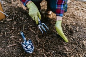 A person wearing gloves using garden tools in soil for planting.