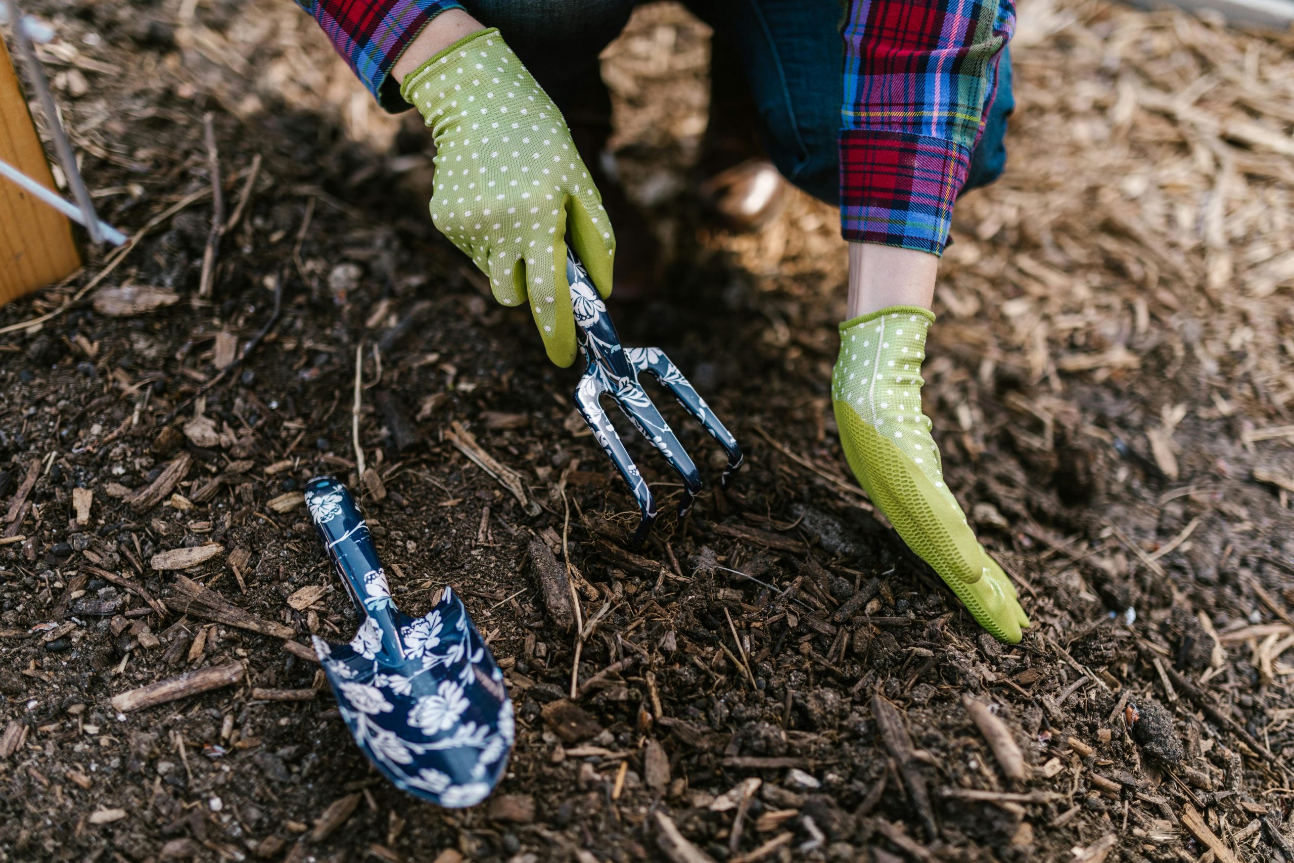 A person wearing gloves using garden tools in soil for planting.