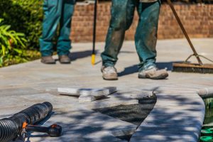 Workers laying tiles on an outdoor patio under sunlight.