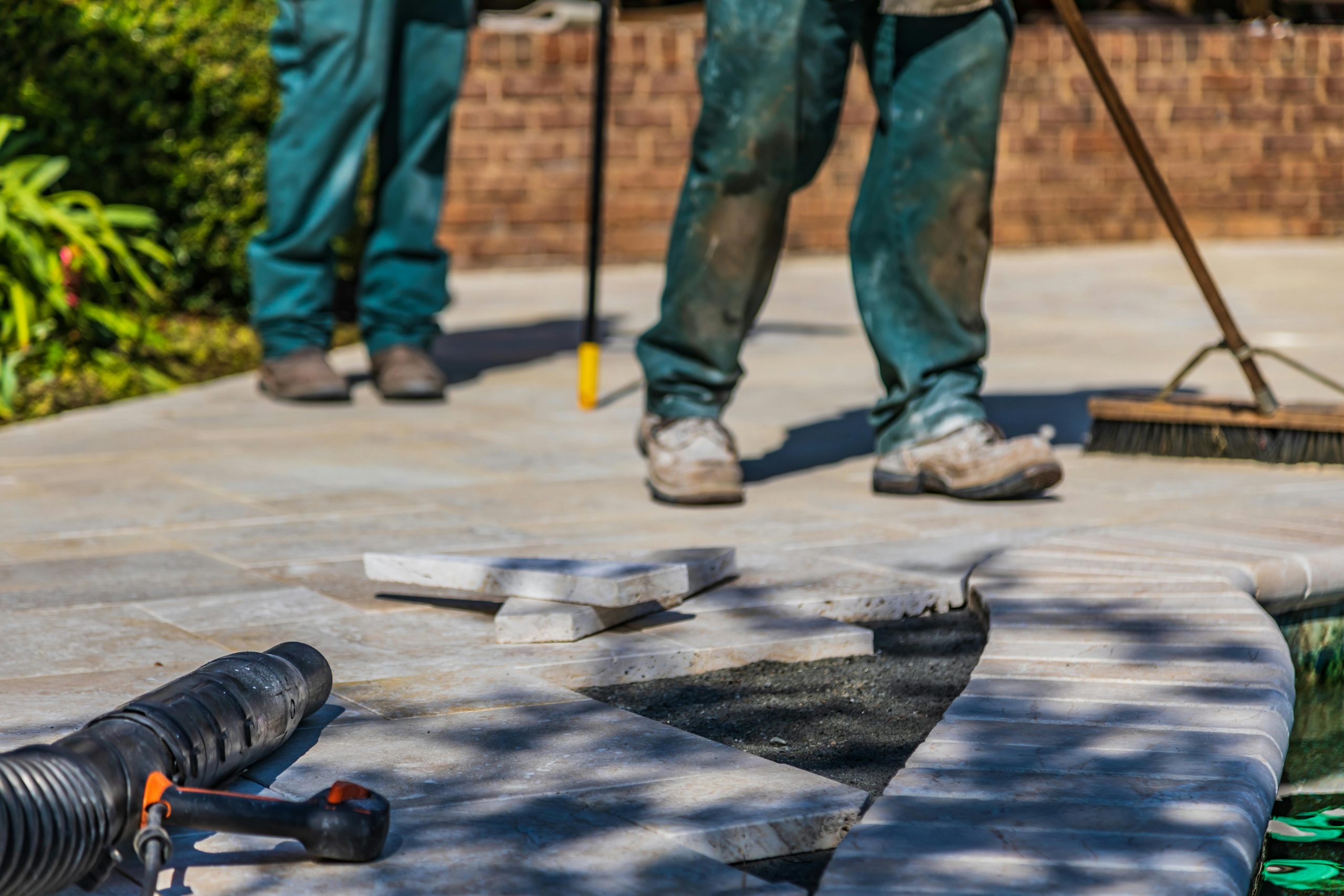 Workers laying tiles on an outdoor patio under sunlight.
